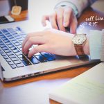 kelloa käyttävä henkilö kirjoittaa kannettavalla tietokoneella.