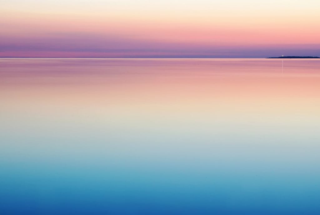 a sunset over the ocean with a small island in the distance