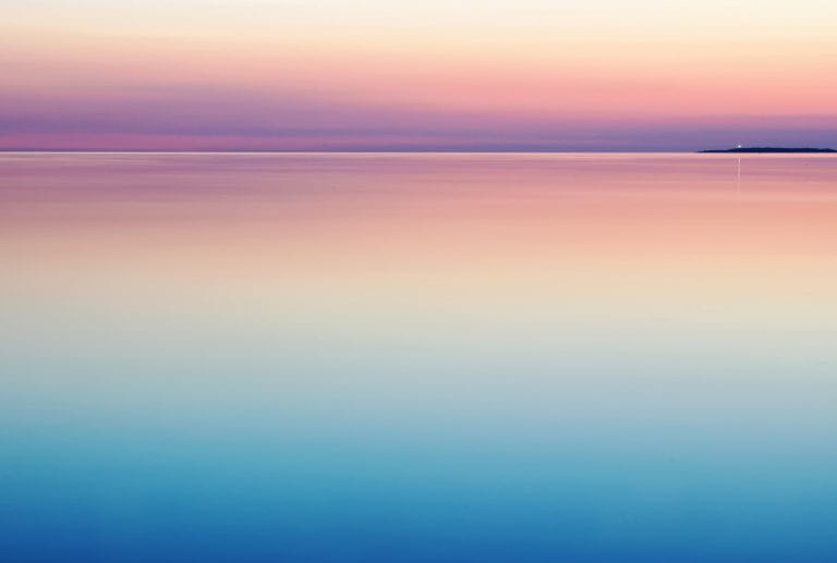 a sunset over the ocean with a small island in the distance