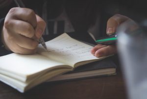 a person is writing in a notebook with a green mobile phone