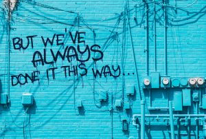 Blue brick wall with graffiti saying 'But we've always done it this way' representing outdated spreadsheet-based sales processes and resistance to CRM adoption