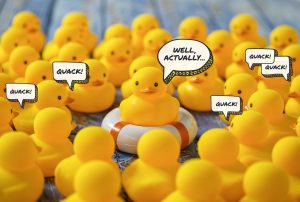 yellow rubber ducks with speech bubbles that say quack and one speech bubble above the middle duck that says well actually