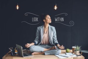 a woman sits in a lotus position on a desk with the words look within behind her