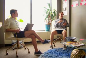 Andy Fowler and Chris Cain sit in chairs with their legs crossed with laptops