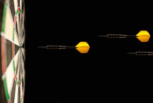 three yellow darts are flying towards the center of a dart board