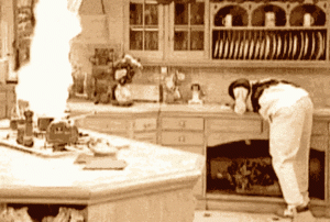 a black and white photo of a kitchen with a fire coming out of the oven