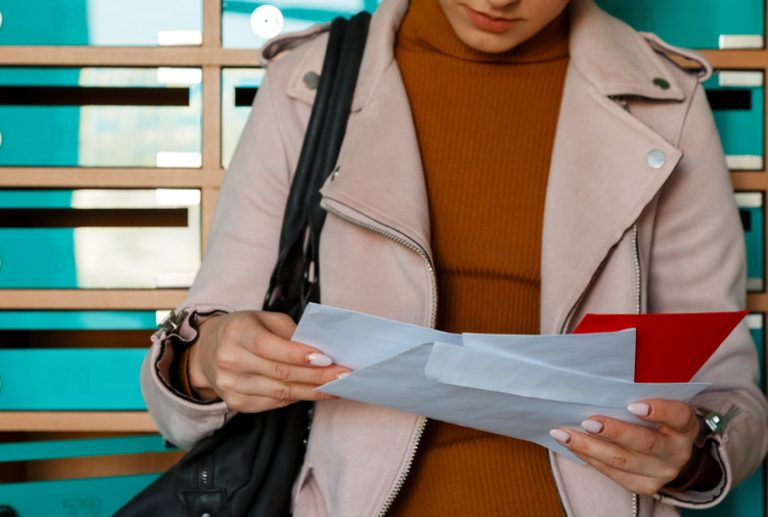 a woman in a pink jacket is holding and looking at envelopes