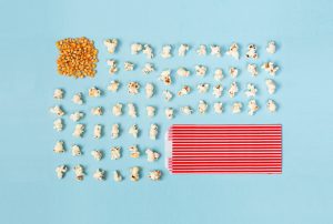 a red and white striped bag of popcorn sits next to a pile of popcorn