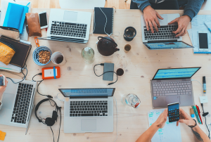 a group of people are sitting at a table with laptops and phones