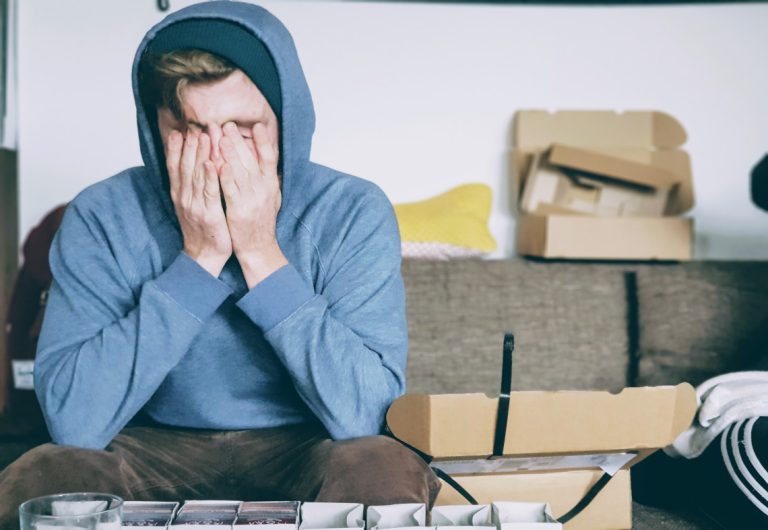 a man in a blue hoodie covering his face with his hands