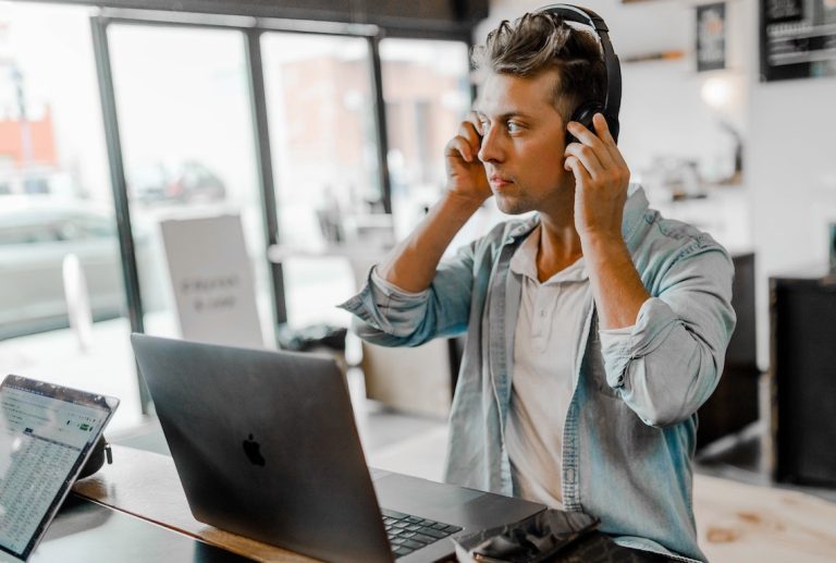 a man wearing headphones sits in front of an apple laptop