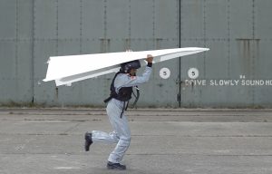 a man carrying a paper airplane in front of a wall that says drive slowly