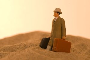 a figurine of a man carrying two suitcases in the sand