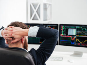 a man sitting in front of two computer monitors with his hands behind his head