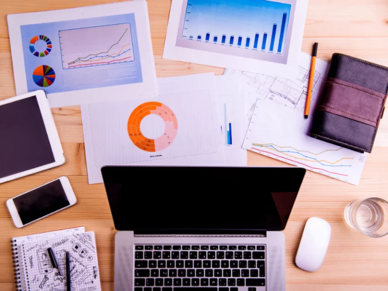 a laptop is open on a wooden desk surrounded by papers and graphs