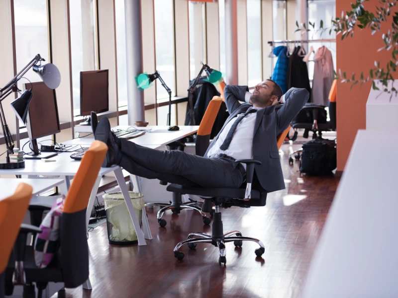 een man leunt achterover in een bureaustoel met zijn voeten op het bureau