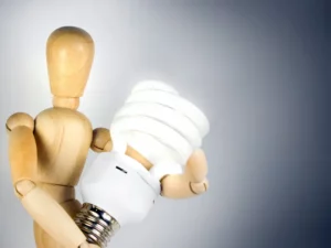 a wooden mannequin is holding a light bulb