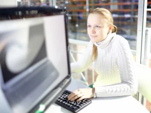 a woman in a white sweater is typing on a keyboard in front of a computer monitor