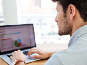 a man is typing on a laptop with a pie chart on the screen
