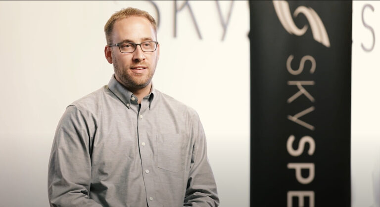 a man stands in front of a sign that says Sky Spec