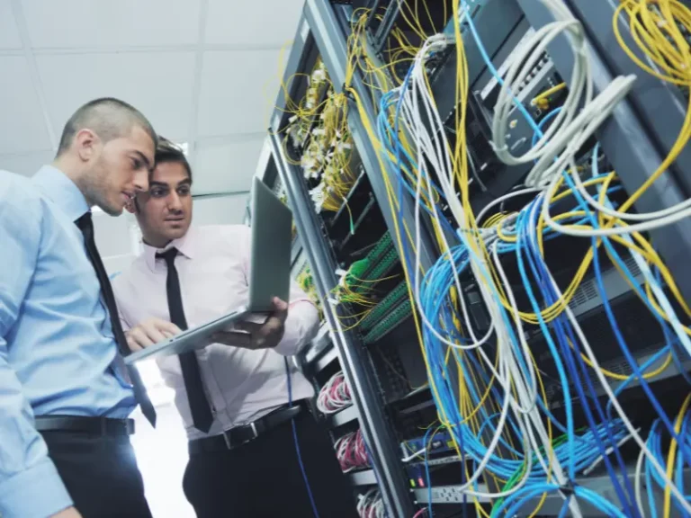 two men looking at a laptop in a server room