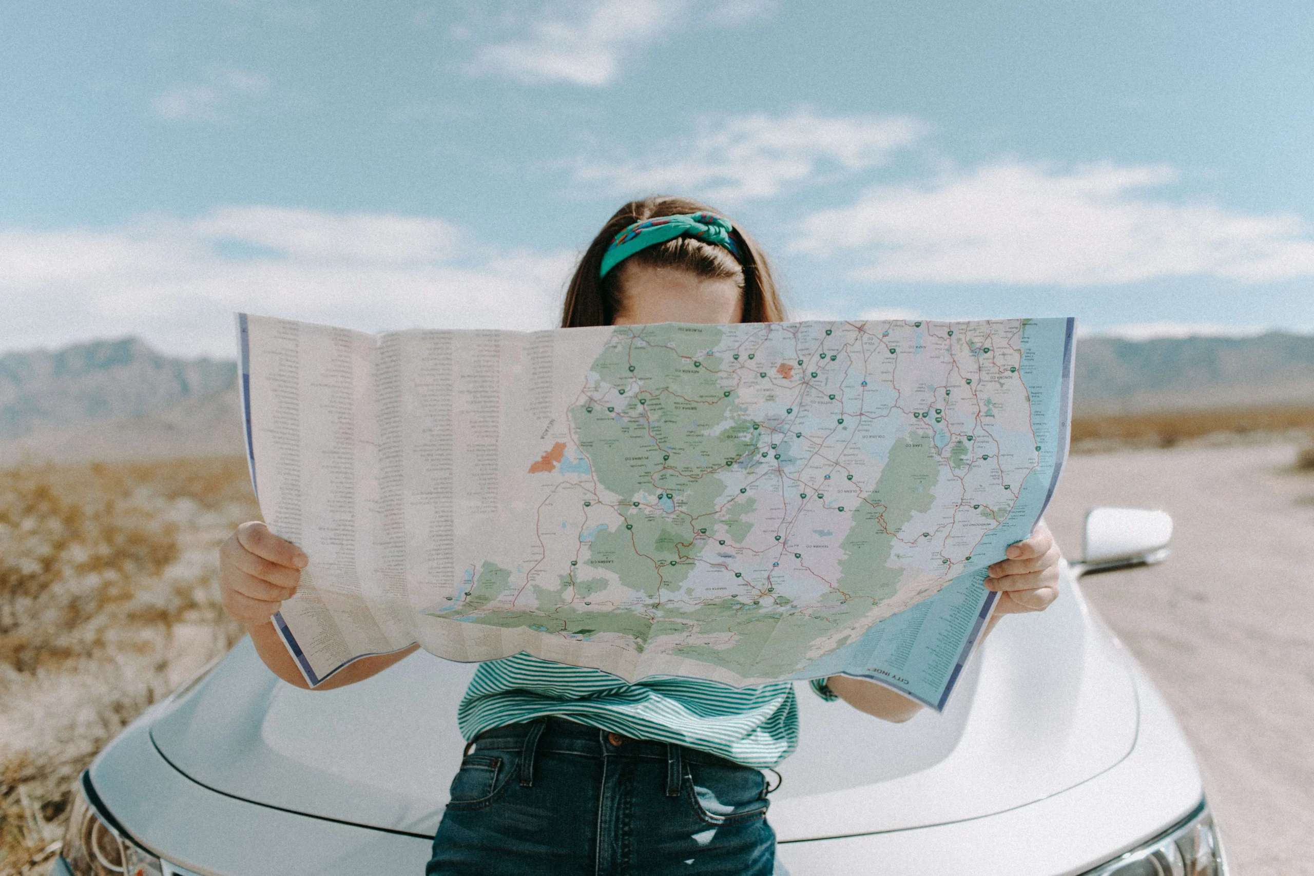 woman leaning on a car holding a map