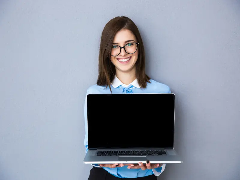 a woman wearing glasses is holding a laptop computer in her hands .