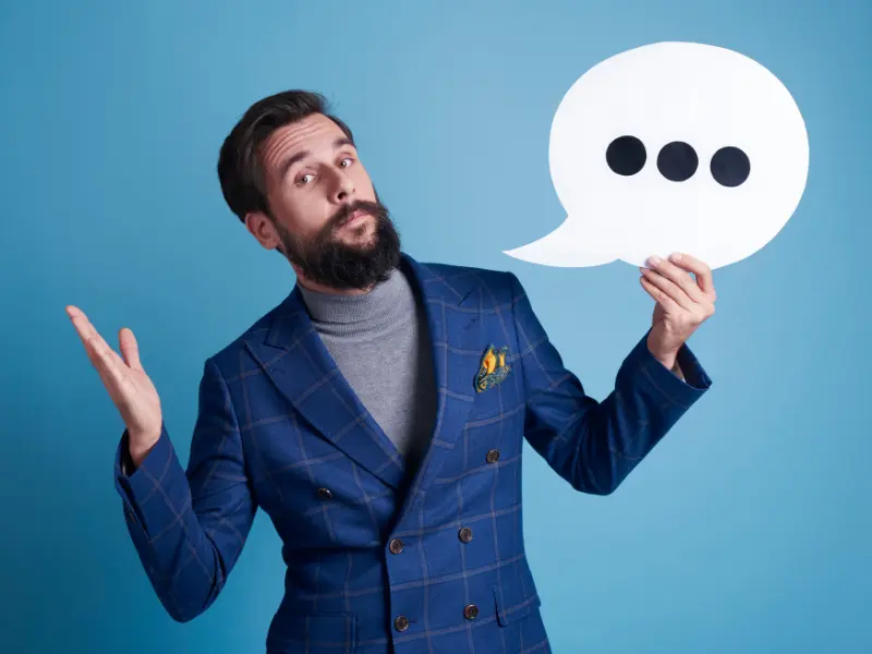 ein Mann im Anzug hält eine Sprechblase mit drei Punkten in der Hand