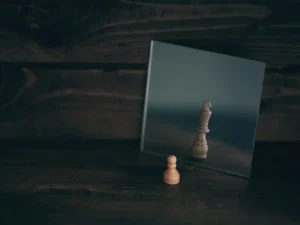 a wooden chess piece is reflected in a mirror on a wooden table .