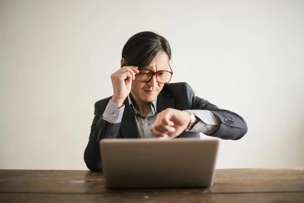 confused businessman with a laptop looking at his watch