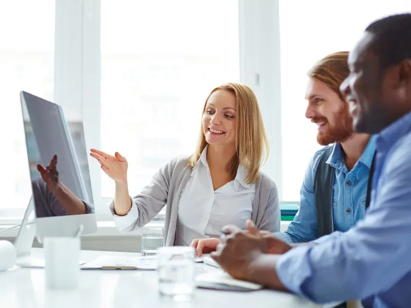 three people face a computer monitor while talking to each other