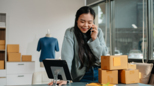 a small business owner talking on the phone with a tablet and boxes in front of her