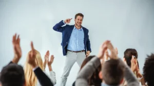 a guy in suit doing a motivational speech on stage and people clapping their hands